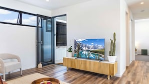 Un salon moderne doté d’un grand téléviseur à écran plat, d’une console en bois et offrant une vue sur les montagnes grâce à une porte-fenêtre coulissante.