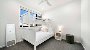 A room with a bunk bed, a bedside table with a lamp, a small stool, and a door.