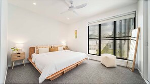 A bedroom with a bed, bedside tables, a ceiling fan, a window with blinds, and a small stool. - Habitat - Lush Lennox Head Apartment (Lennox Head)