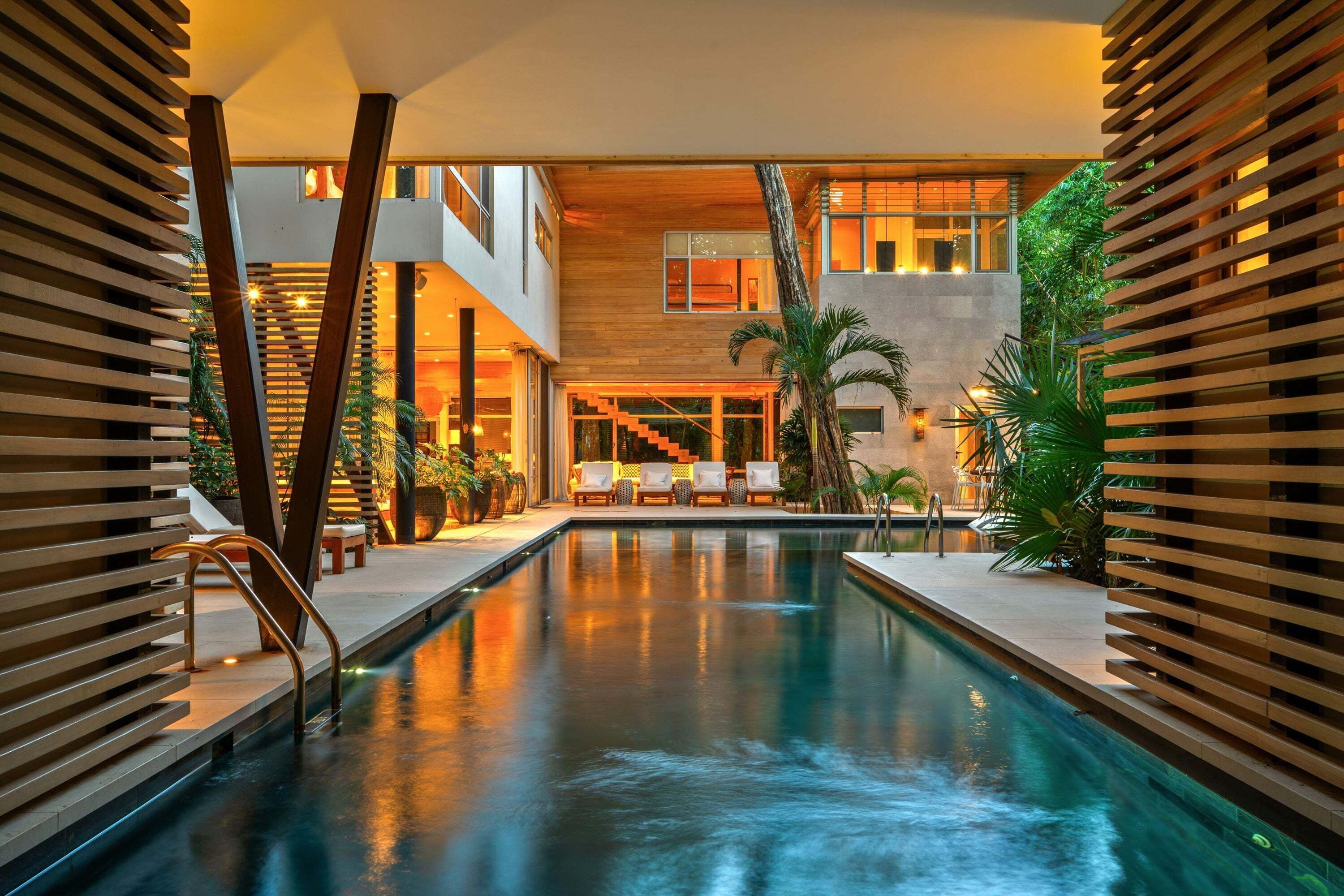 Une piscine intérieure moderne avec vue sur un immeuble à plusieurs étages, un espace détente et des plantes tropicales.
