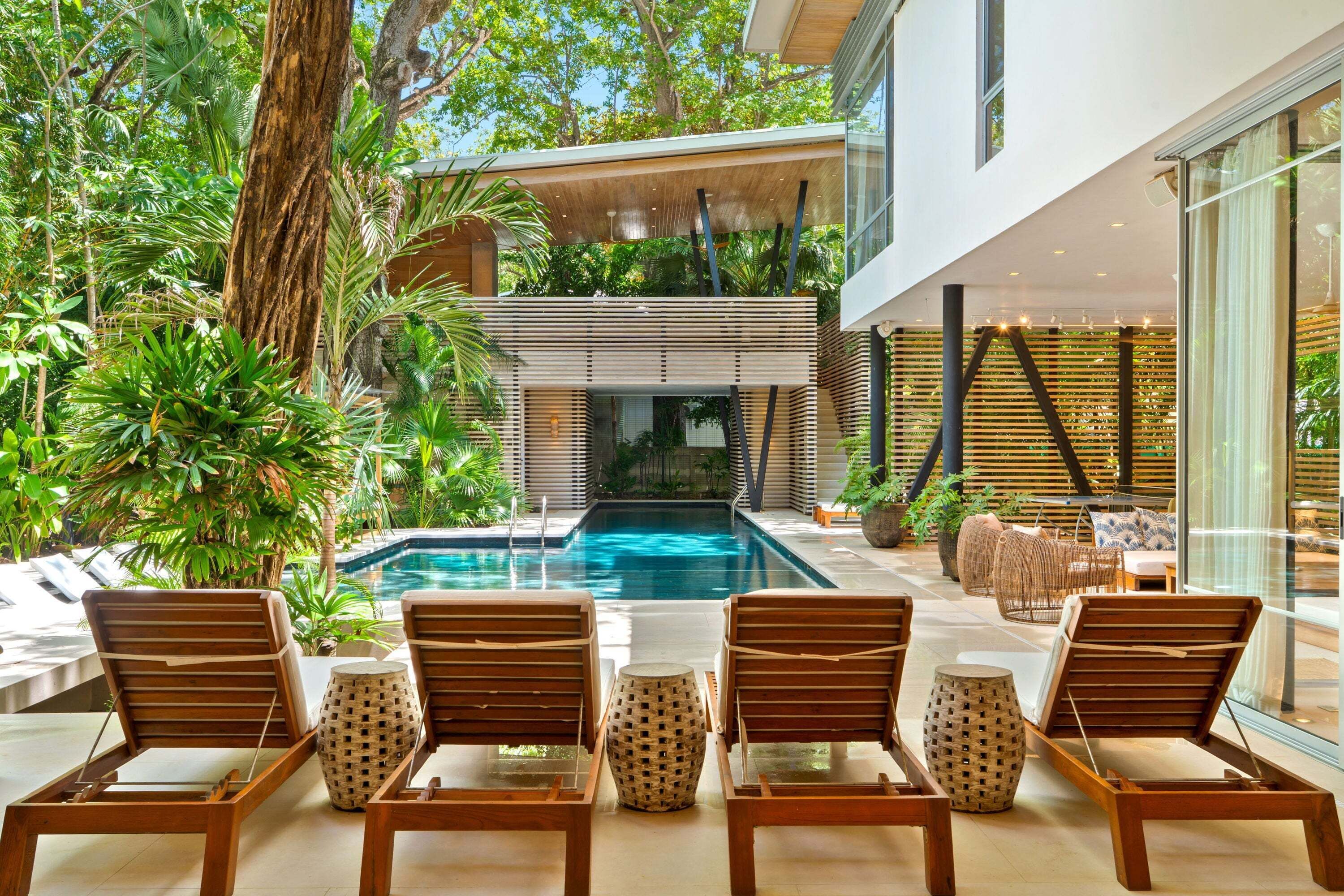 Un área junto a la piscina con sillones de descanso, una piscina y abundante vegetación.