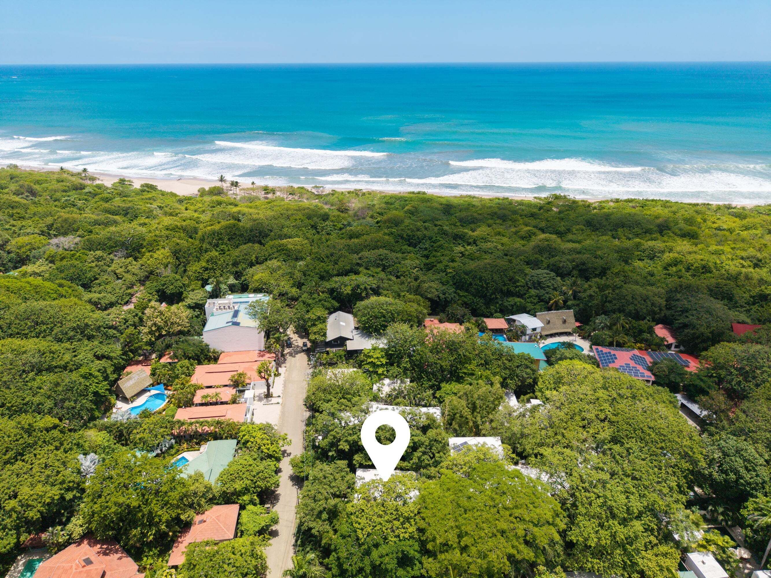 An aerial view of a coastal resort with multiple buildings surrounded by dense greenery, a beach, and the ocean.