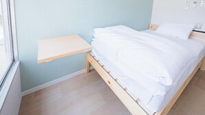 Una cama individual con ropa de cama blanca en una habitación con paredes azul claro y suelo de madera.