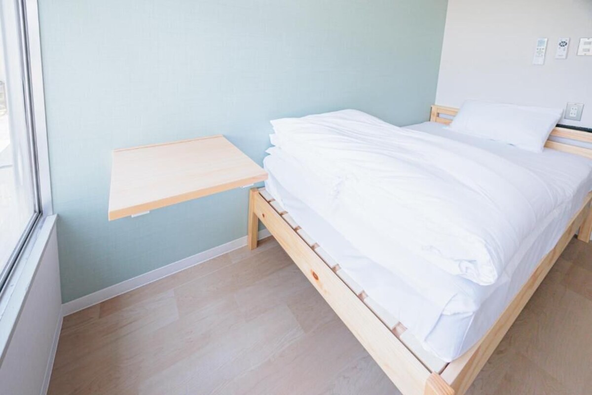 A single bed with white bedding in a room with light blue walls and a wooden floor.