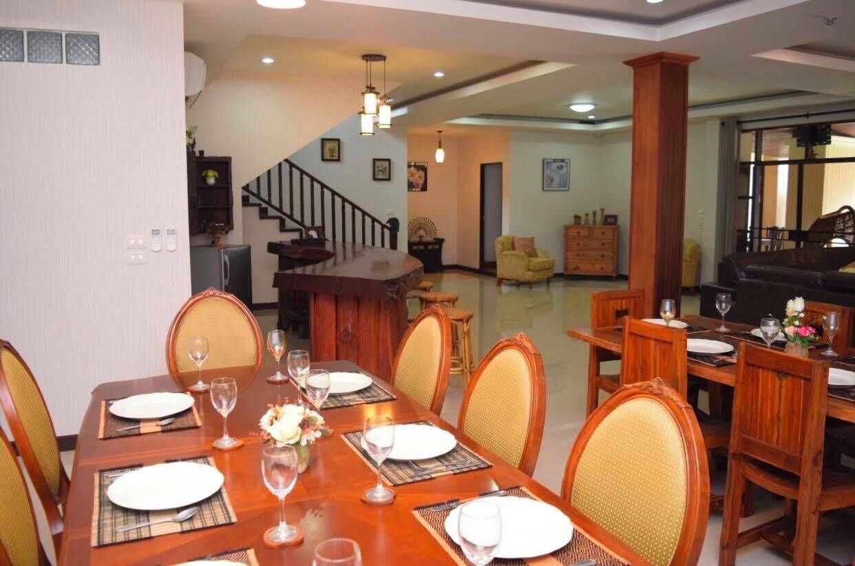 Uma sala de jantar com mesa de madeira posta para seis lugares, cadeiras e escada que leva a outro cômodo.