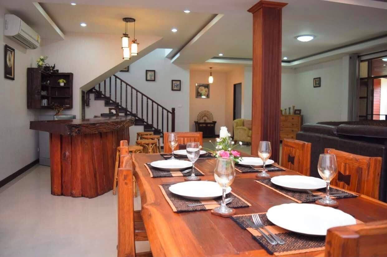 Un coin repas avec une table en bois dressée pour quatre personnes, un escalier et, au fond, un salon.