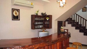 Eine Bar mit Holztresen, Korbsesseln, einem Glaskasten und einer Treppe im Hintergrund.