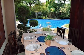 Mesa posta para refeição, vista para uma piscina e vegetação.