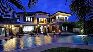 A multi-story house with a swimming pool, outdoor seating, and a well-lit balcony.