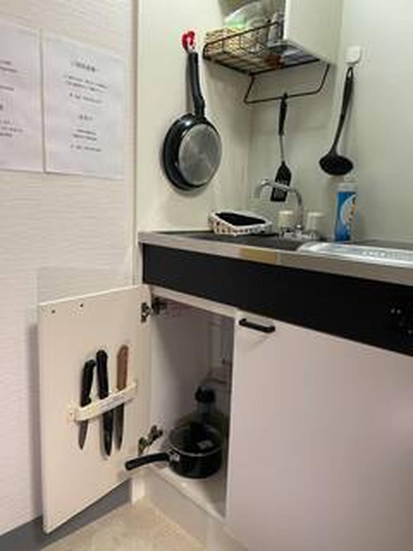 A kitchen with a black countertop, a white cabinet, and a black pot under the sink.