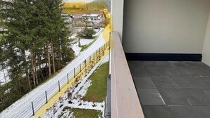 A balcony with a view of a snow-covered landscape, a fence, and a building in the background. - Lisa Apartment in Hinterstoder, Ski-In Ski-Out (Hinterstoder)