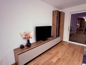Un saló modern amb un moble de roba de fusta, un televisor de pantalla plana i un ram de flors seques.