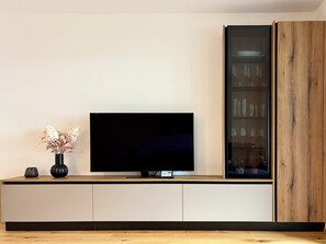 A flat-screen TV on a wooden cabinet with a glass display unit to the right.