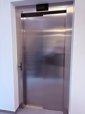 A metallic elevator door with a control panel and a no-smoking sign.
