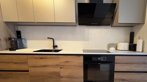 A modern kitchen with wooden cabinets, a black dishwasher, and a built-in oven. - Lisa Apartment in Hinterstoder, Ski-In Ski-Out (Hinterstoder)