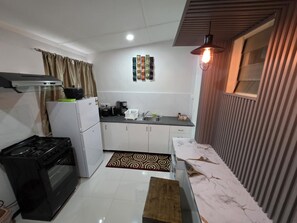 A compact kitchen with a gas stove, a refrigerator, and a microwave. There is a patterned rug on the floor and a wooden table with a marble countertop.