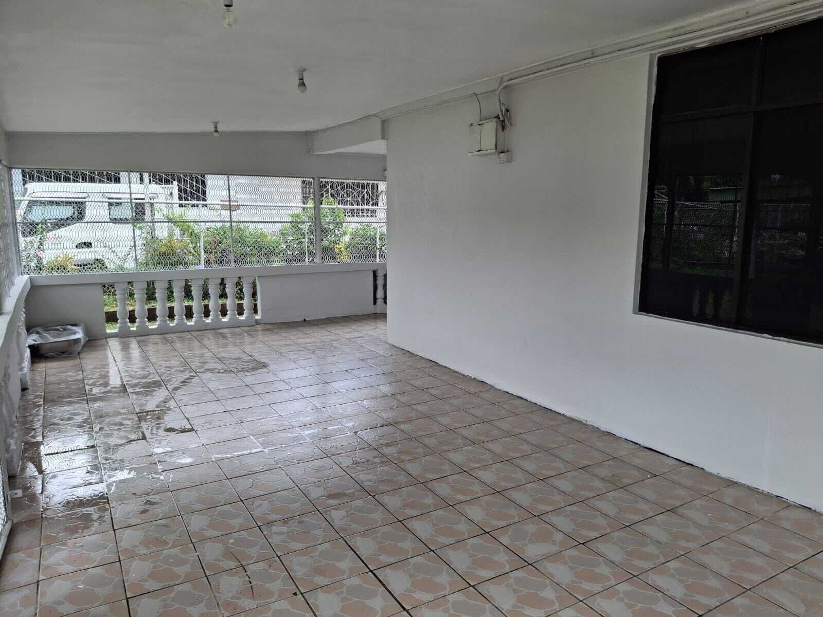 Varanda limpa com azulejos, grade branca e uma janela grande.