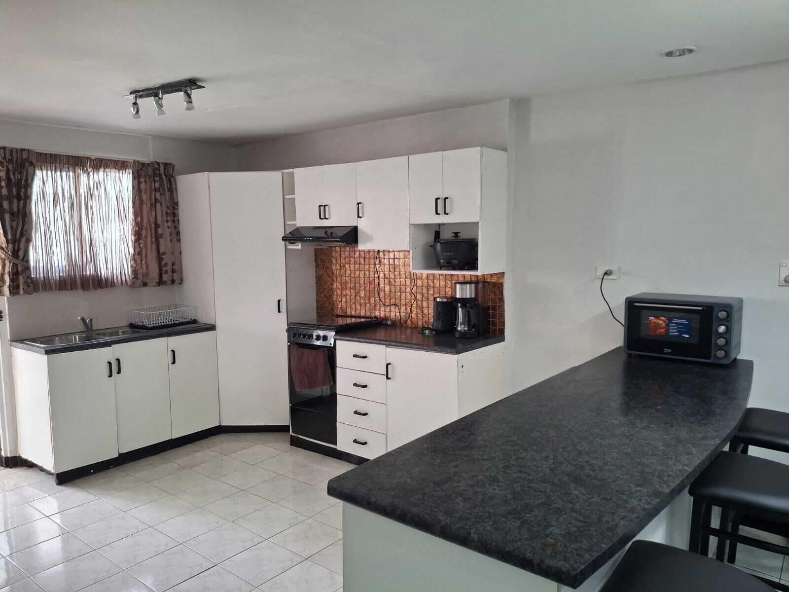 Una cocina compacta con gabinetes blancos, estufa, microondas y cafetera.