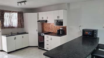 A compact kitchen with white cabinets, a stove, a microwave, and a coffee maker.