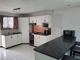 Una cocina compacta con gabinetes blancos, estufa, microondas y cafetera.