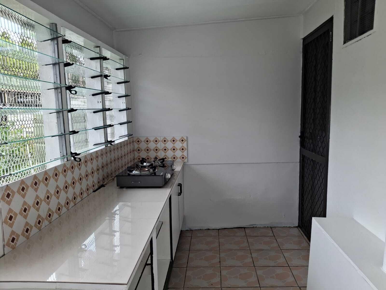 Uma cozinha compacta com fogão a gás, armários brancos e azulejos estampados.