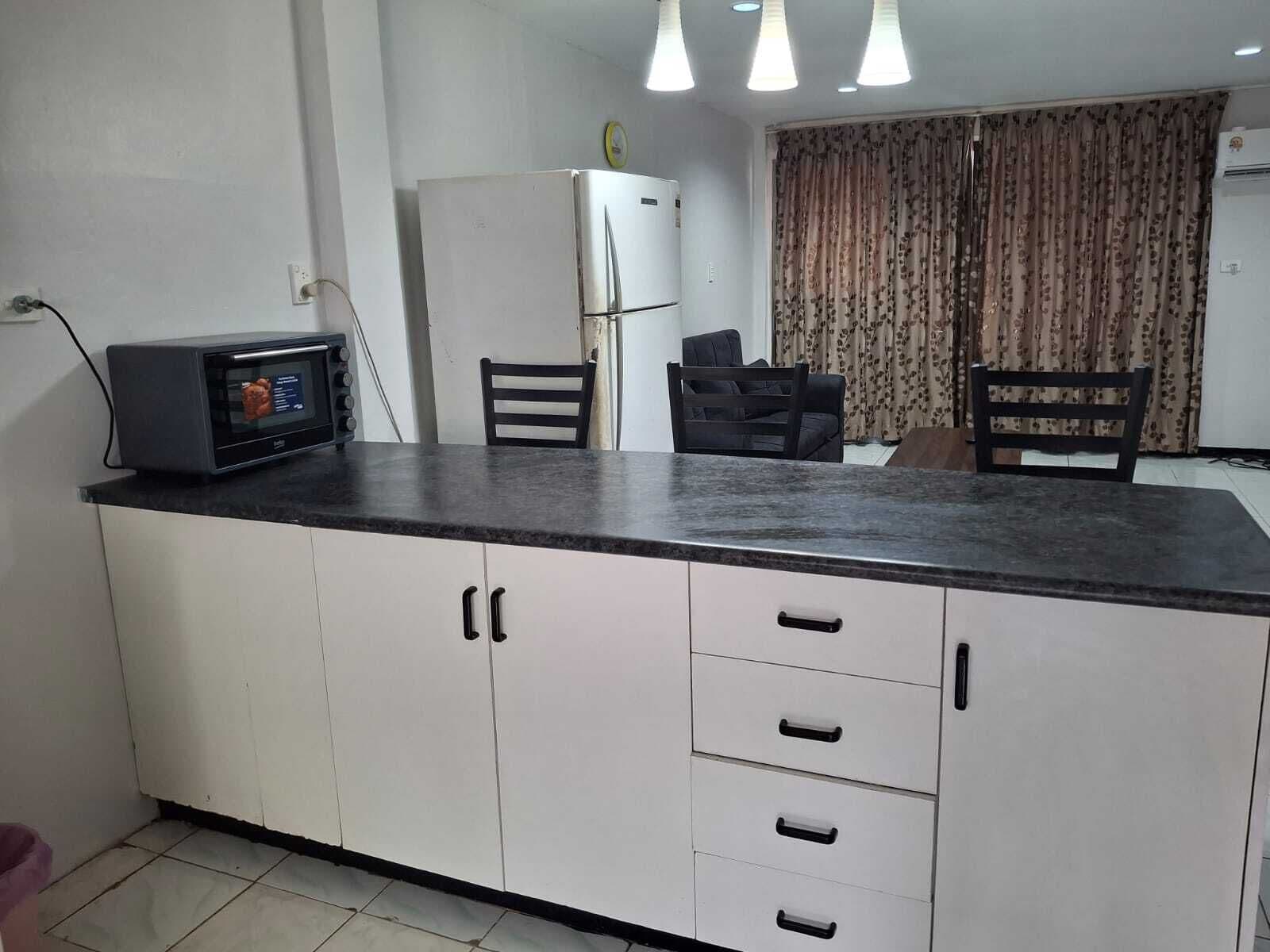 A kitchen with white cabinets, a black countertop, a microwave, and a refrigerator.