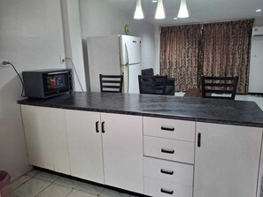 A kitchen with white cabinets, a black countertop, a microwave, and a refrigerator. - PVV Nadi Airport Apartment  (Nadi)