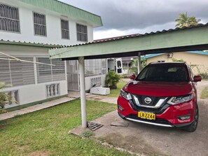 A red Nissan SUV parked under a covered area with a white building in the background. - PVV Nadi Airport Apartment  (Nadi)