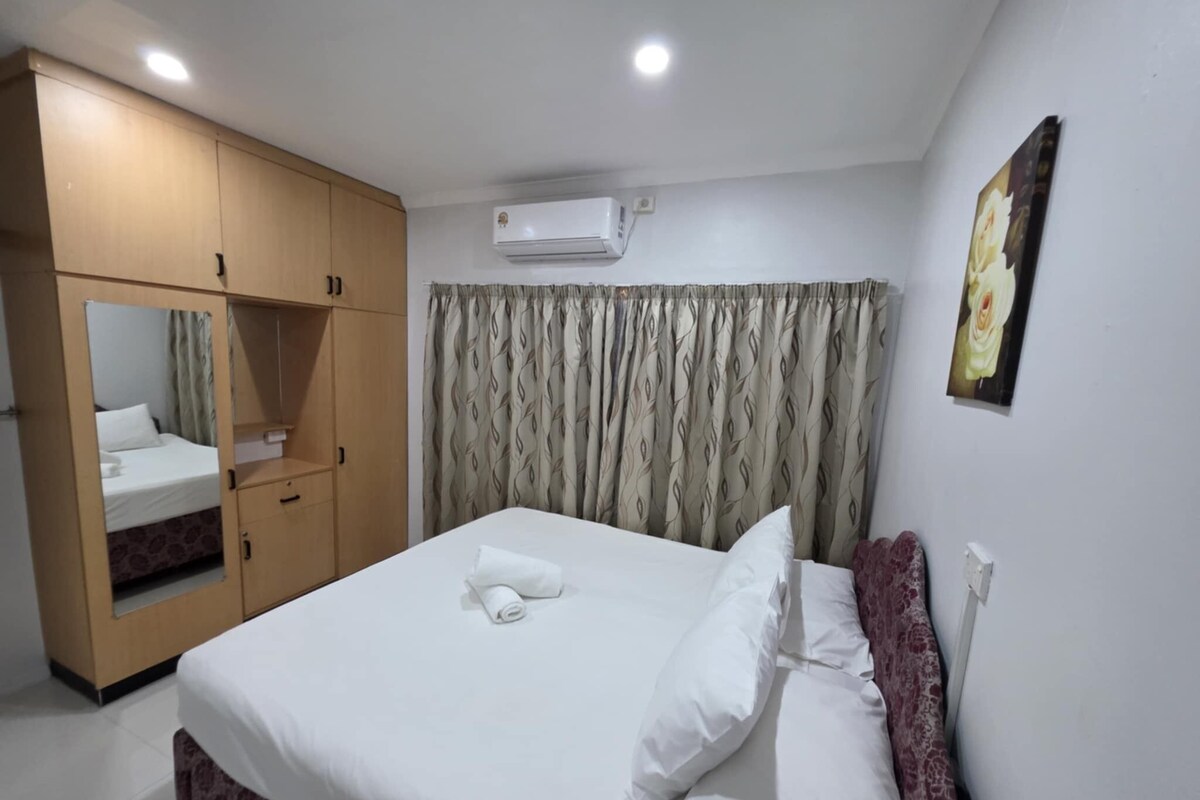 A hotel room with a bed, a wardrobe, a mirror, an air conditioner, and a painting on the wall.