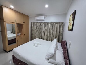 A hotel room with a bed, a wardrobe, a mirror, an air conditioner, and a painting on the wall.