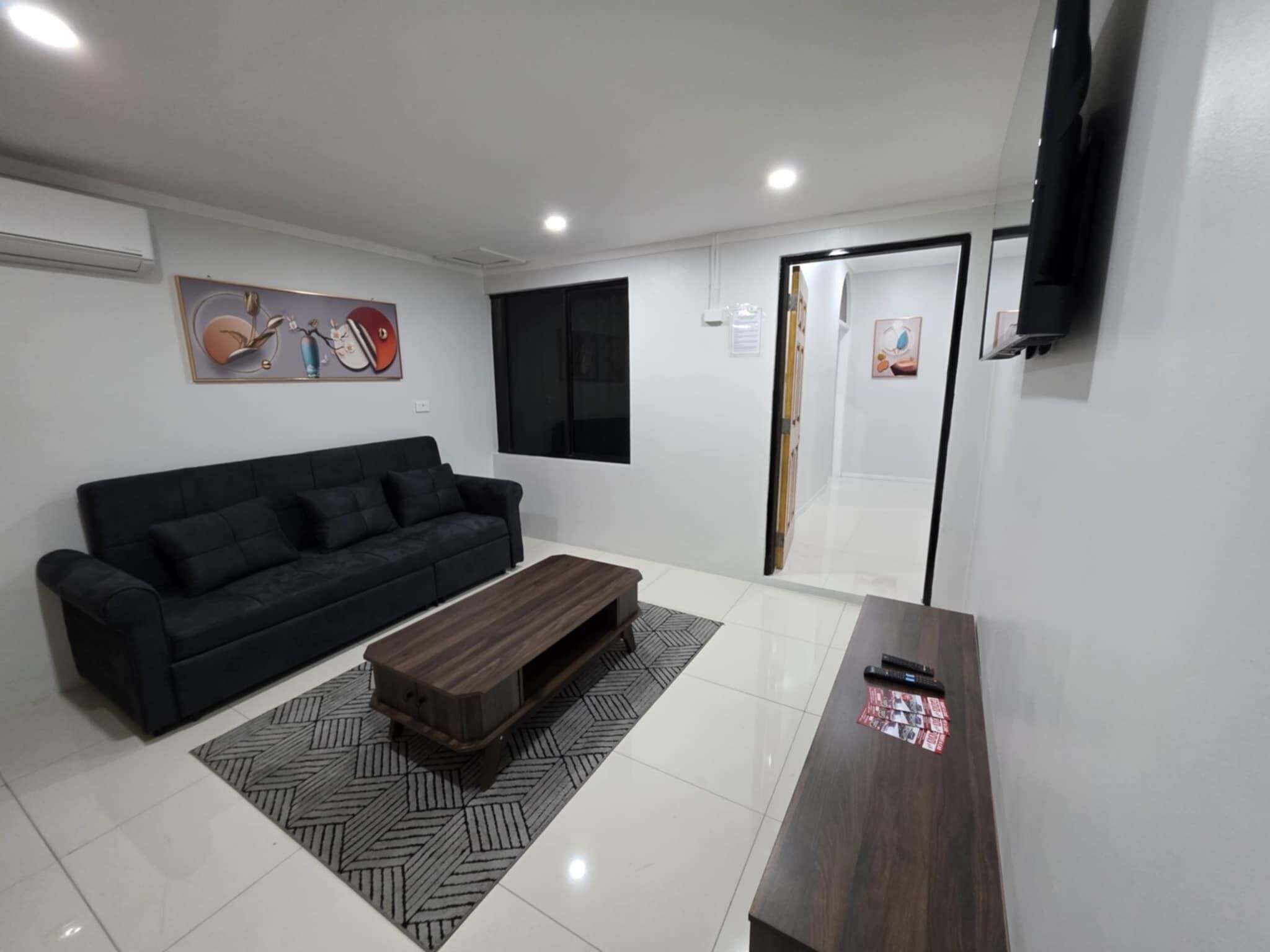 A modern living room with a black sofa, a wooden coffee table, and a TV mounted on the wall.