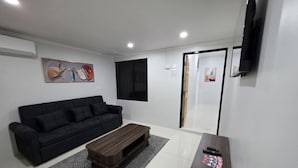 Una sala de estar moderna con un sofá negro, una mesa de centro de madera y un televisor montado en la pared.