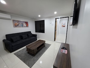 A modern living room with a black sofa, a wooden coffee table, and a TV mounted on the wall.
