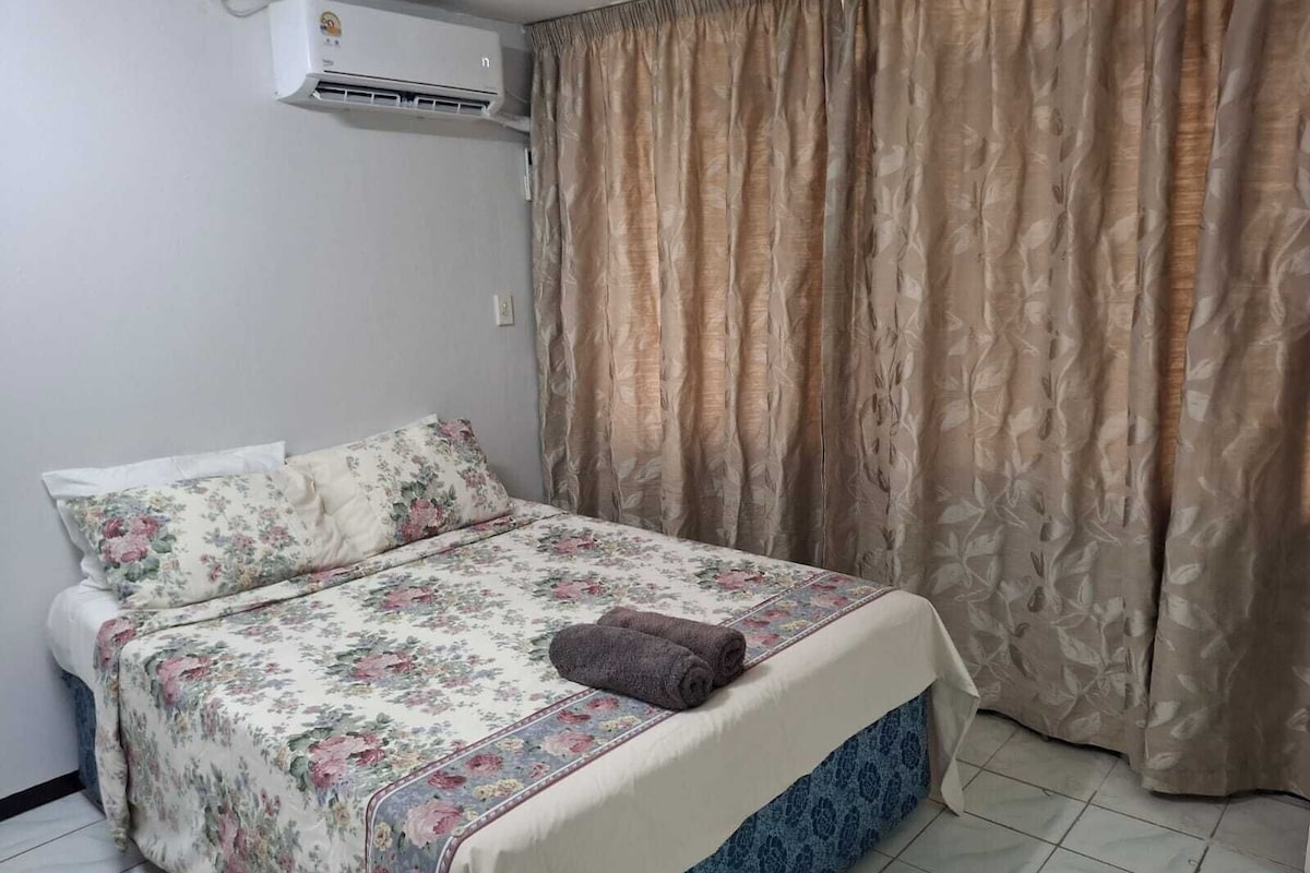 A single bed with floral bedding, a brown towel, and a blue skirted bed base.