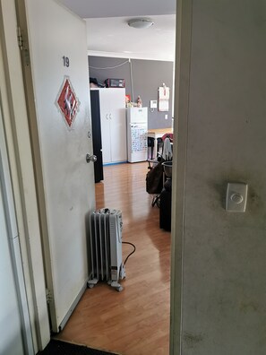 A hallway with a white door labeled '19', a white refrigerator, a small heater, and a wall-mounted phone. - Room- Cozy Guest Room in Regents Park (Regents Park)