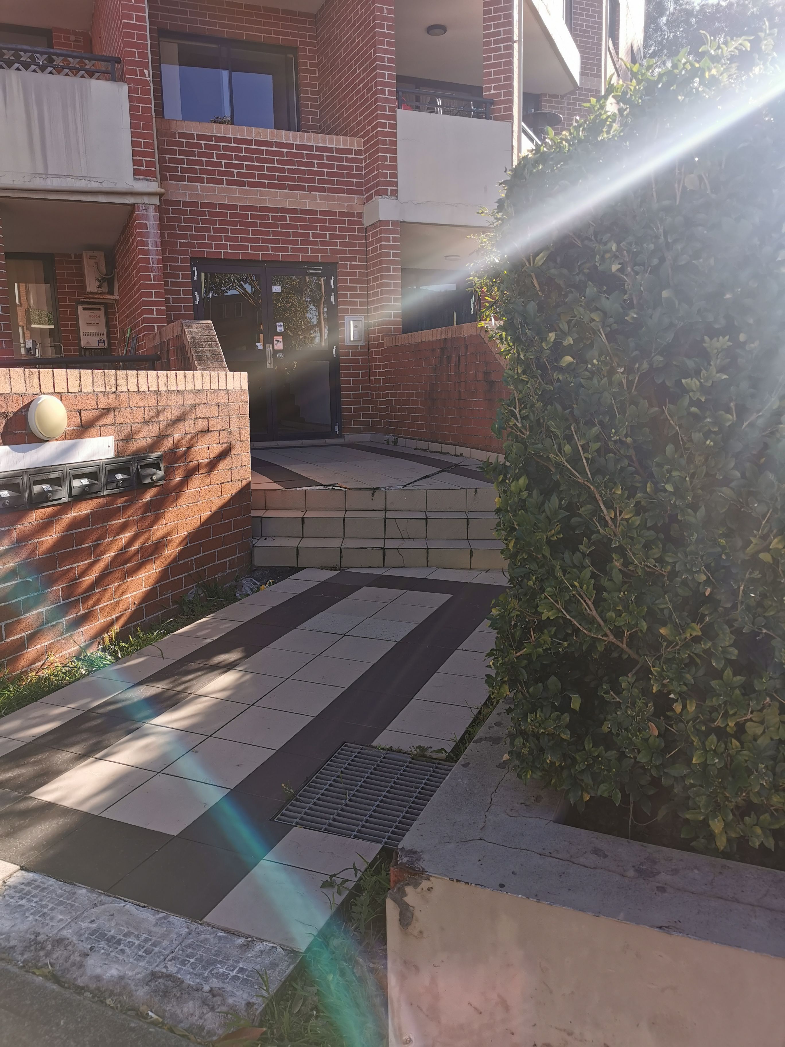 A courtyard with a brick building, a tiled floor, and a planter with greenery.