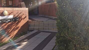 A courtyard with a brick building, a tiled floor, and a planter with greenery.