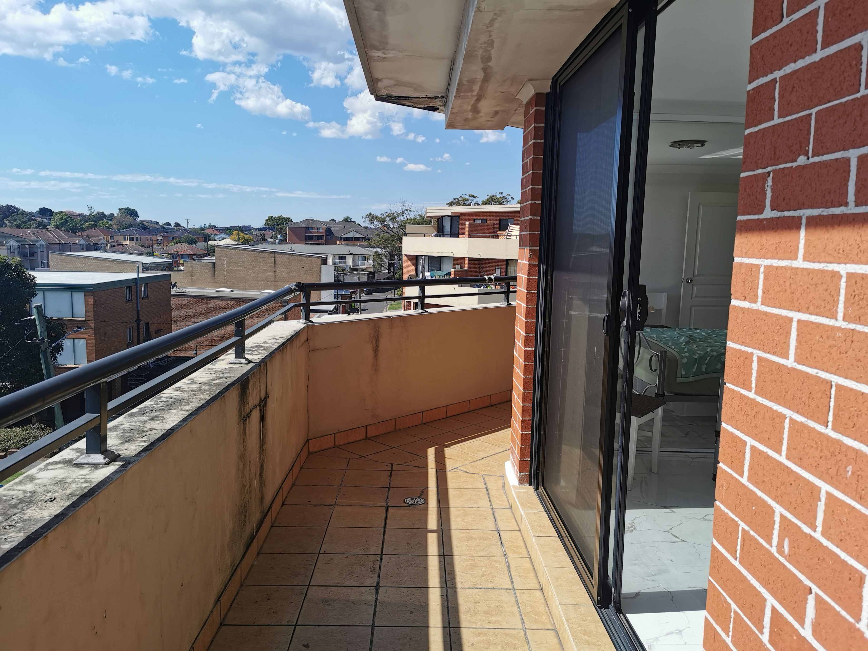 A balcony with a tiled floor, a metal railing, and a glass door leading to an interior space.