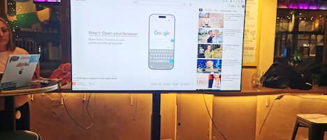 A computer monitor displaying a Google homepage with a smartphone image, a laptop, and a sign for 'What's On' in the background.