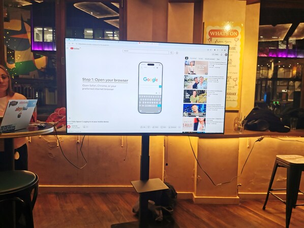 A computer monitor displaying a Google homepage with a smartphone image, a laptop, and a sign for 'What's On' in the background.