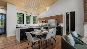 A modern kitchen with wooden ceiling, large windows, and a dining area with a table set for four. - Luxe Cabin with Heated Indoor Pool, Hot Tub, Arcade & Theater near Dollywood (Sevierville)