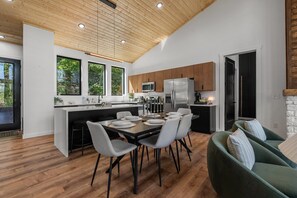 A modern kitchen with wooden ceiling, large windows, and a dining area with a table set for four. - Luxe Cabin with Heated Indoor Pool, Hot Tub, Arcade & Theater near Dollywood (Sevierville)