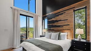 A modern bedroom with a large bed, a nightstand, a dresser, and a view of the outdoors. - Luxe Cabin with Heated Indoor Pool, Hot Tub, Arcade & Theater near Dollywood (Sevierville)