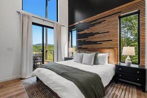 A modern bedroom with a large bed, a nightstand, a dresser, and a view of the outdoors. - Luxe Cabin with Heated Indoor Pool, Hot Tub, Arcade & Theater near Dollywood (Sevierville)