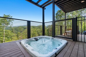A hot tub on a wooden deck with a view of a forested landscape. - Luxe Cabin with Heated Indoor Pool, Hot Tub, Arcade & Theater near Dollywood (Sevierville)