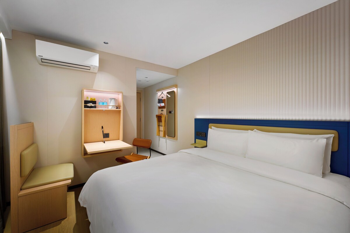 Una habitación de hotel con una cama, un escritorio, una silla, un espejo y un armario.