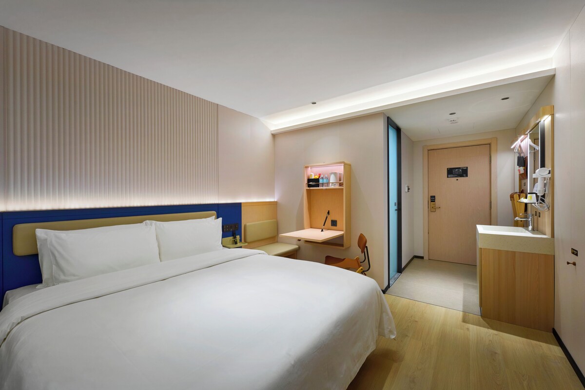 Una habitación de hotel con cama, mesita de noche y baño pequeño con lavabo y espejo.
