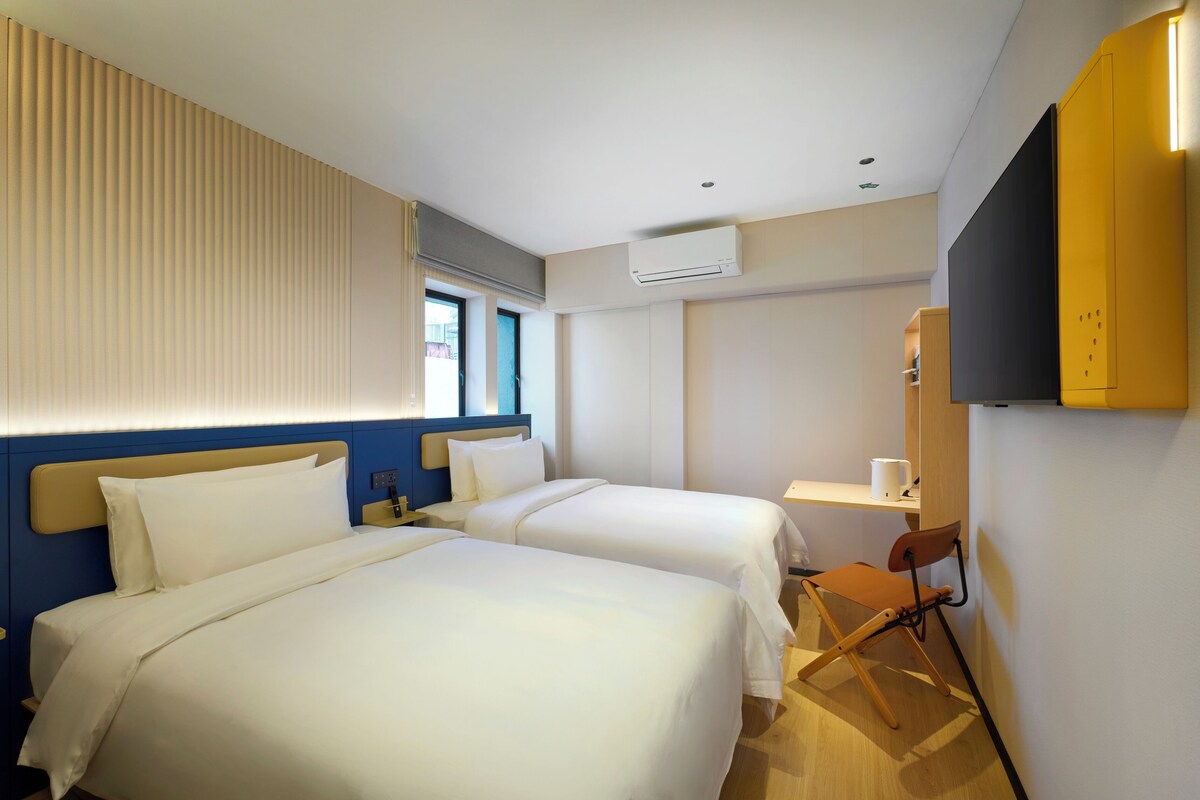 Habitación de hotel con dos camas, un escritorio, una silla, un equipo de aire acondicionado y un televisor.