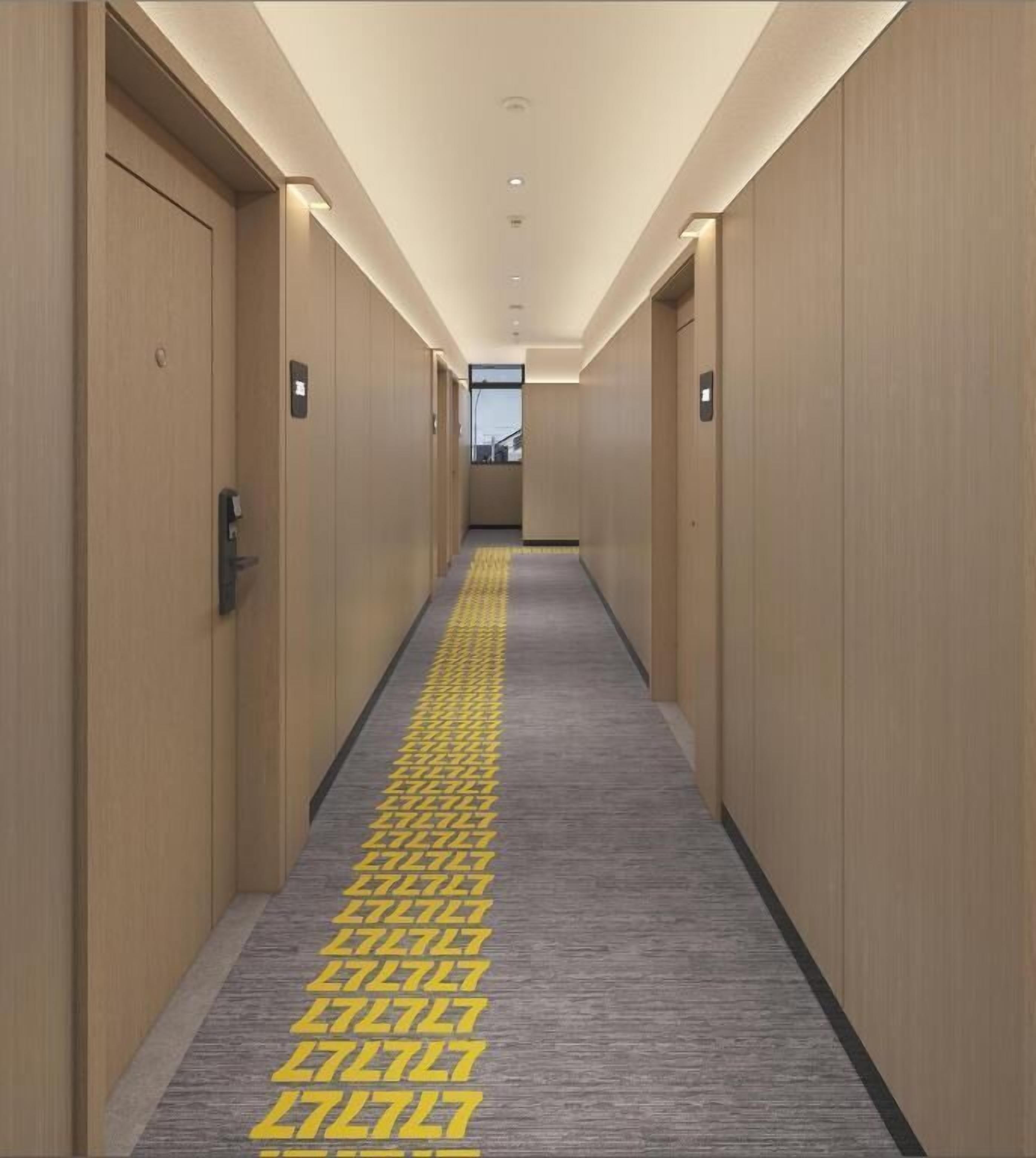 Un pasillo de hotel con puertas de madera, alfombra estampada y piso de color claro.