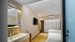 Una habitación de hotel con baño, cama, televisor y ventana con cortinas.